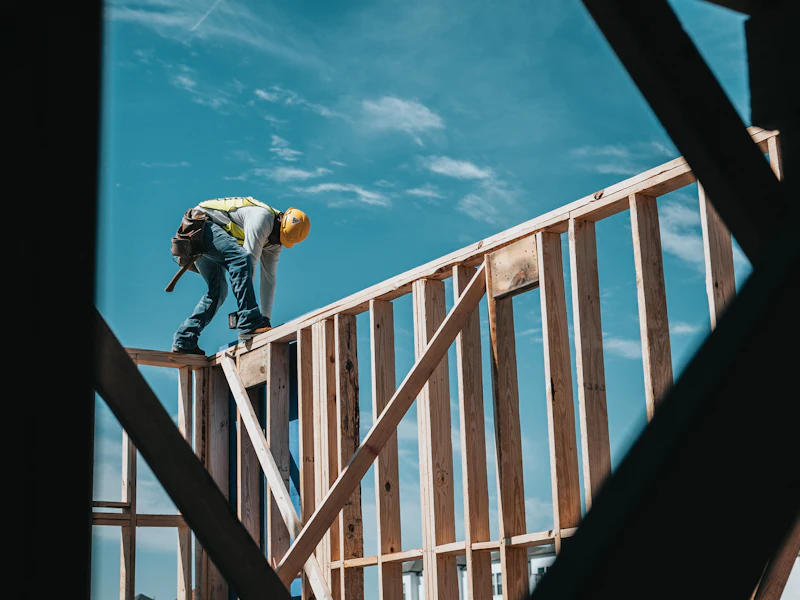 Worker fixing the timber frame of a low-rise building against a blue sky